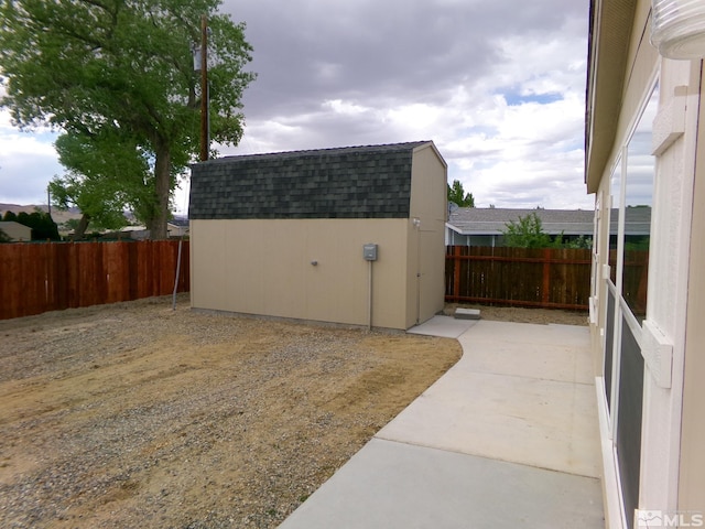 view of side of home with a patio, a fenced backyard, roof with shingles, and a storage shed