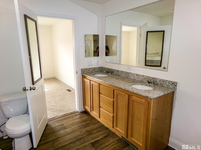 full bathroom with a sink, toilet, double vanity, and wood finished floors
