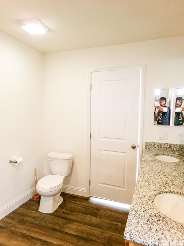bathroom with double vanity, wood finished floors, a sink, baseboards, and toilet