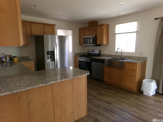 kitchen with dark wood-style flooring, light stone countertops, a sink, a peninsula, and stainless steel appliances