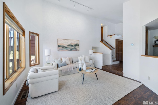living area with dark wood-style flooring, visible vents, rail lighting, stairway, and baseboards