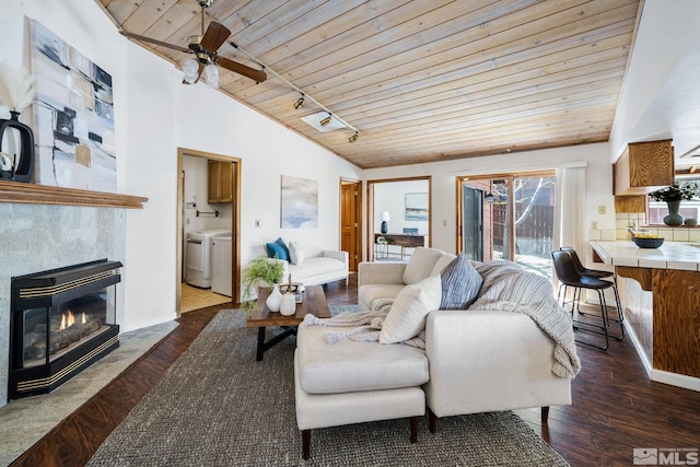 living area with ceiling fan, dark wood-type flooring, vaulted ceiling, washing machine and dryer, and wood ceiling