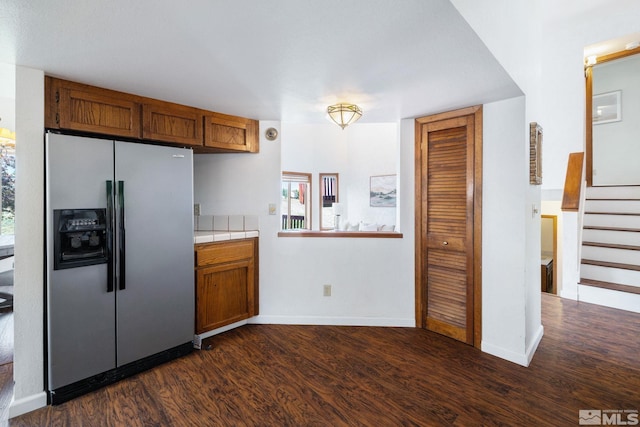kitchen with brown cabinets, stainless steel fridge with ice dispenser, baseboards, tile counters, and dark wood-type flooring