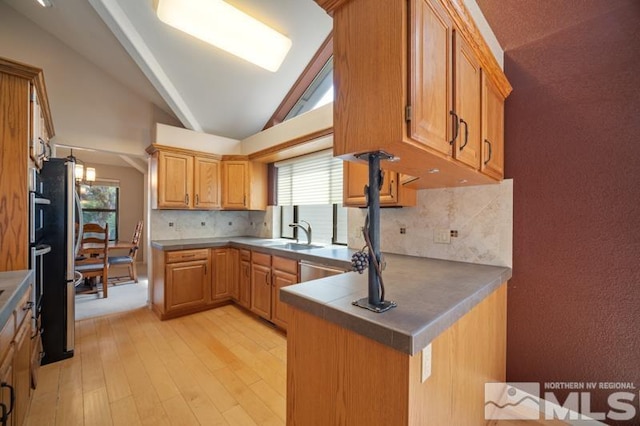 kitchen with a peninsula, light wood-type flooring, a sink, backsplash, and vaulted ceiling