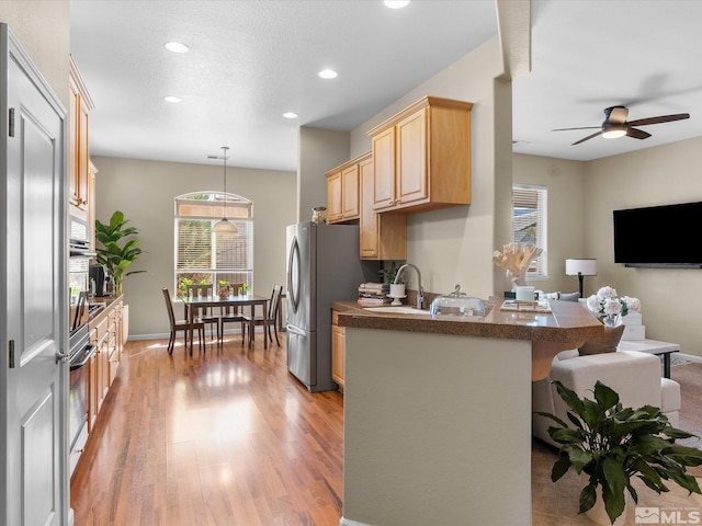 kitchen with a peninsula, light brown cabinetry, dark countertops, light wood-style floors, and open floor plan