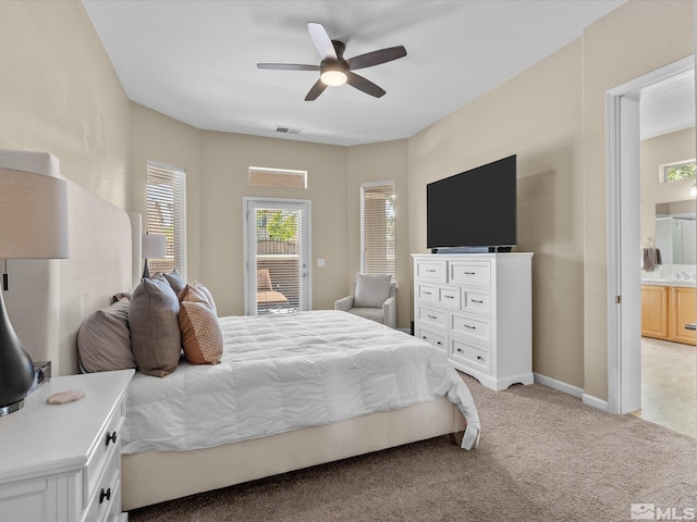 bedroom with ceiling fan, light colored carpet, visible vents, baseboards, and ensuite bathroom