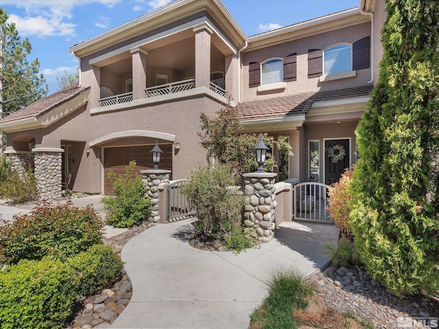 mediterranean / spanish home with a garage, a gate, stucco siding, and a balcony