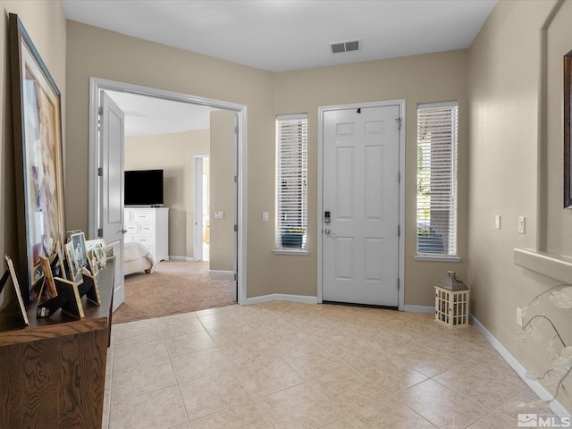 foyer featuring baseboards, visible vents, light carpet, and light tile patterned floors