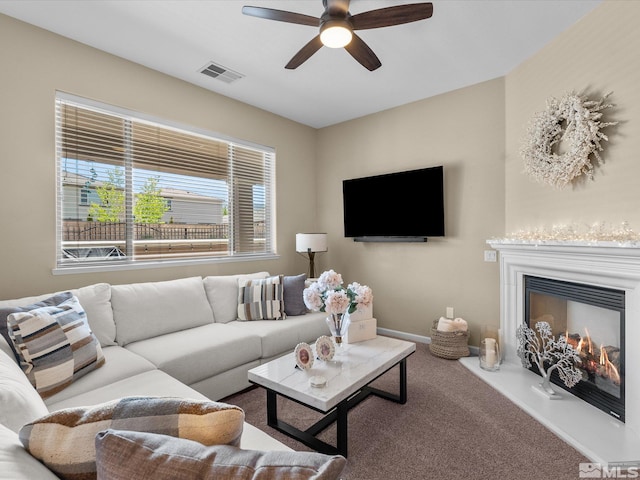 carpeted living room featuring a lit fireplace, ceiling fan, visible vents, and baseboards
