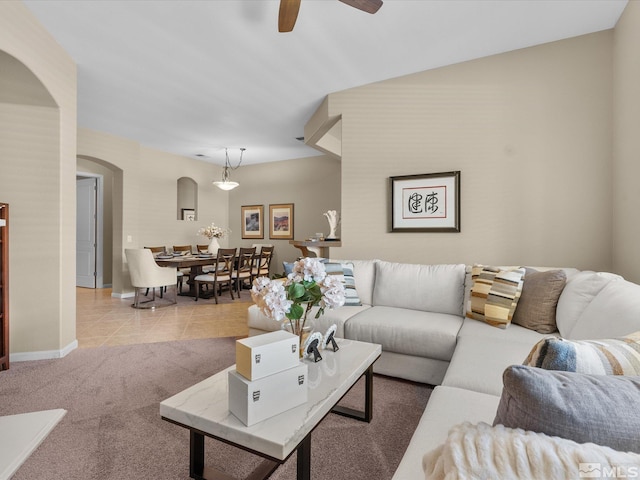 living room with light carpet, arched walkways, a ceiling fan, baseboards, and light tile patterned floors