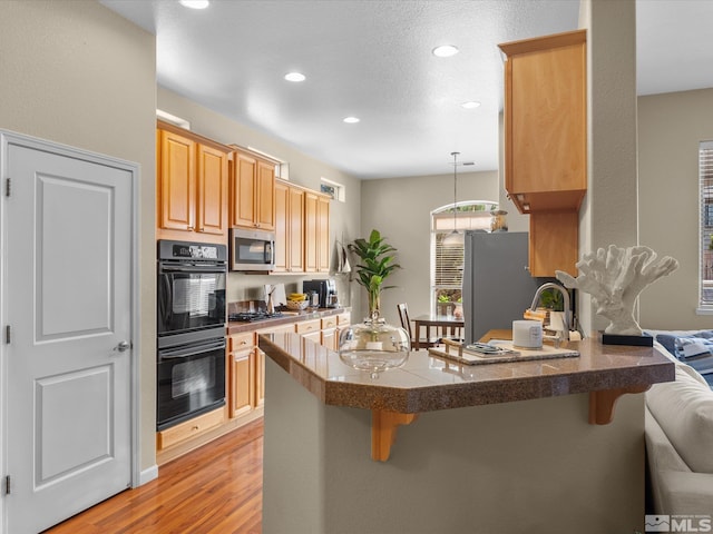 kitchen featuring a kitchen bar, a peninsula, light wood-style floors, stainless steel appliances, and recessed lighting