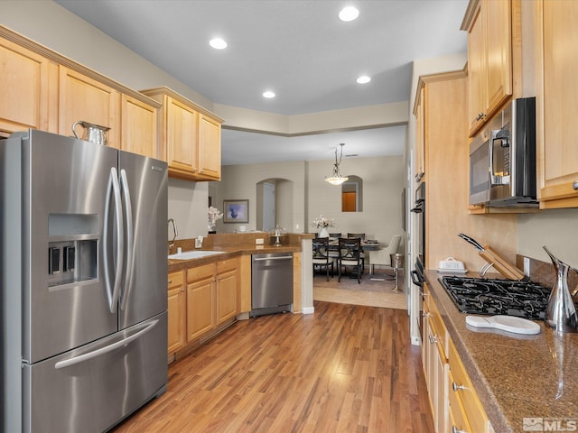 kitchen with a sink, light brown cabinets, arched walkways, stainless steel appliances, and tile countertops