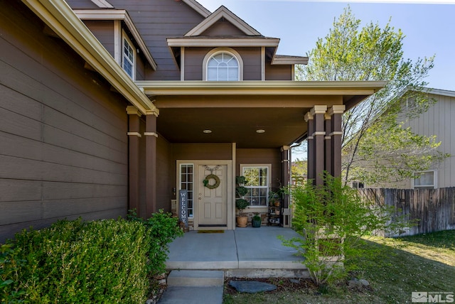 view of exterior entry featuring covered porch and fence