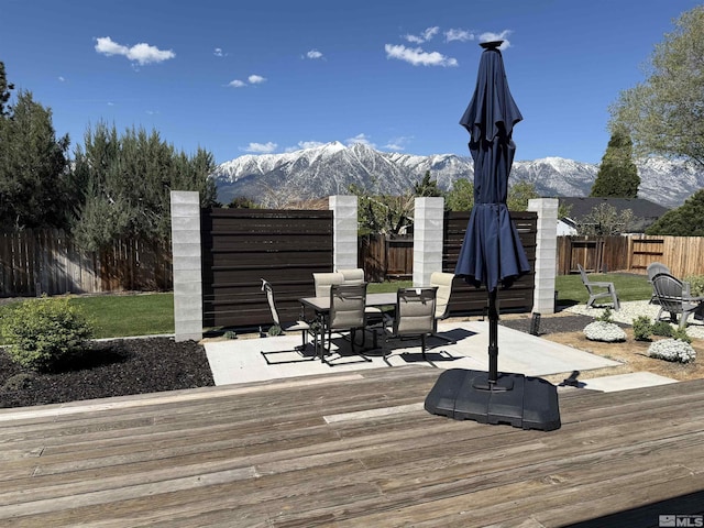 wooden deck featuring outdoor dining area, a fenced backyard, a lawn, and a mountain view
