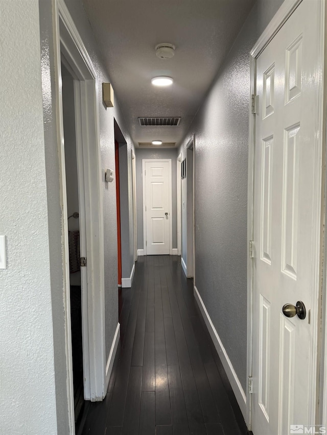 corridor with baseboards, visible vents, a textured wall, and dark wood finished floors