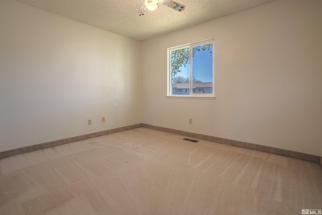 spare room featuring visible vents, a textured ceiling, baseboards, and light carpet