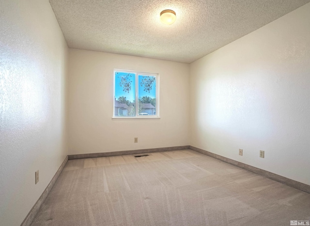 unfurnished room featuring baseboards, light carpet, a textured ceiling, and visible vents