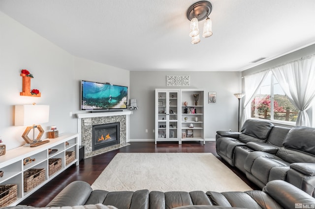 living room with a tiled fireplace, dark wood finished floors, baseboards, and visible vents