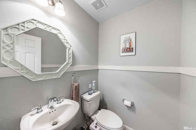 half bath featuring toilet, visible vents, and a sink