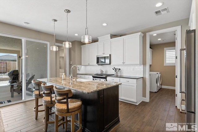 kitchen with backsplash, appliances with stainless steel finishes, a sink, dark wood-style floors, and separate washer and dryer