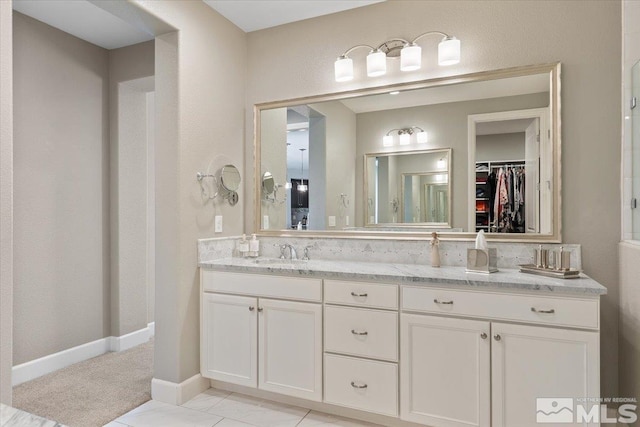 full bathroom with double vanity, a sink, baseboards, and a spacious closet