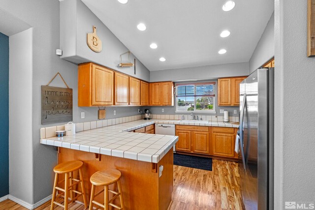 kitchen with a sink, freestanding refrigerator, a peninsula, and light wood-style flooring