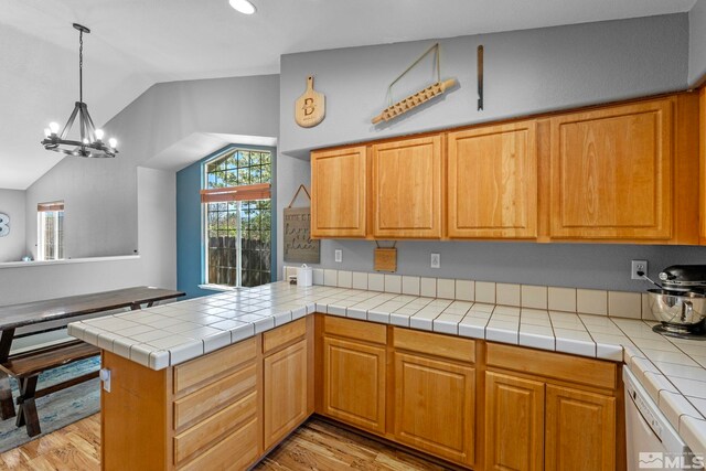 kitchen featuring an inviting chandelier, a peninsula, lofted ceiling, light wood finished floors, and dishwasher
