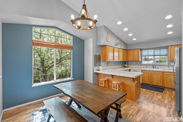 kitchen featuring a sink, freestanding refrigerator, tile countertops, a peninsula, and vaulted ceiling