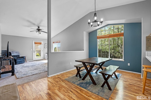 dining space with ceiling fan with notable chandelier, baseboards, vaulted ceiling, and light wood finished floors