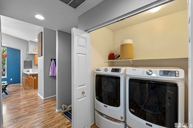 clothes washing area with laundry area, visible vents, washing machine and clothes dryer, light wood-type flooring, and baseboards