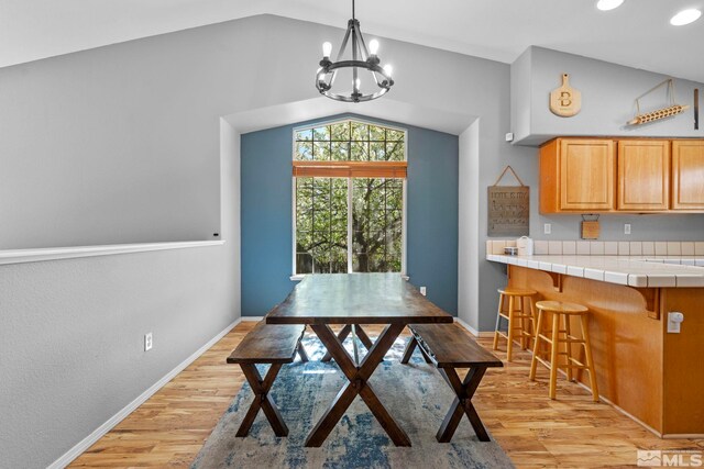 dining area with baseboards, an inviting chandelier, light wood finished floors, and lofted ceiling