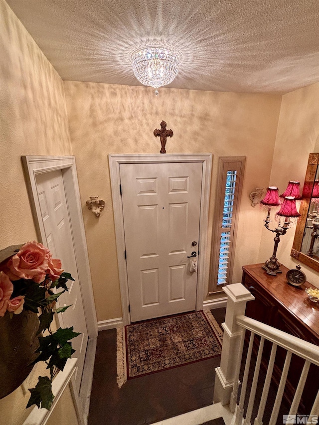 entryway with a textured ceiling, a notable chandelier, and baseboards
