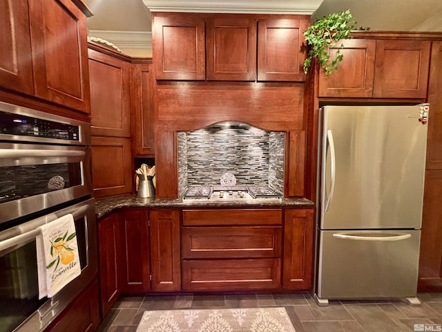 kitchen with brown cabinetry, dark stone counters, backsplash, and stainless steel appliances