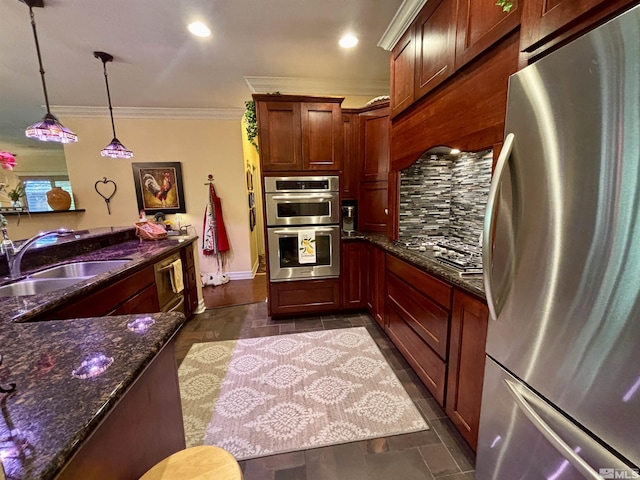 kitchen with hanging light fixtures, a sink, dark stone counters, stainless steel appliances, and ornamental molding