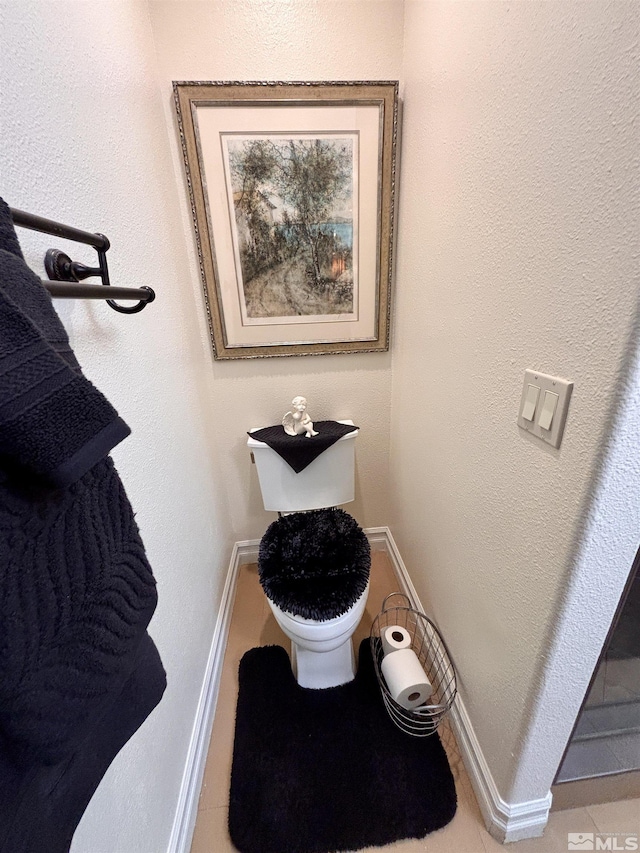 bathroom with toilet, baseboards, and tile patterned flooring