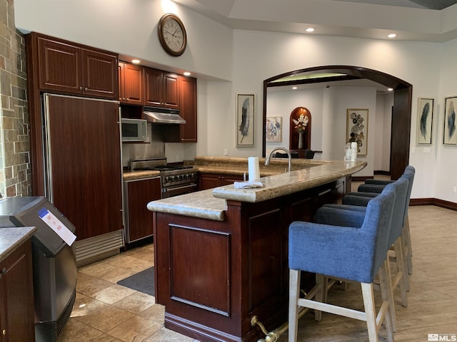 kitchen featuring a breakfast bar, arched walkways, recessed lighting, under cabinet range hood, and high end stainless steel range oven