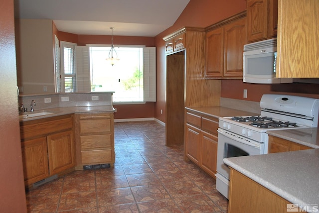 kitchen featuring white appliances, decorative light fixtures, a sink, and light countertops