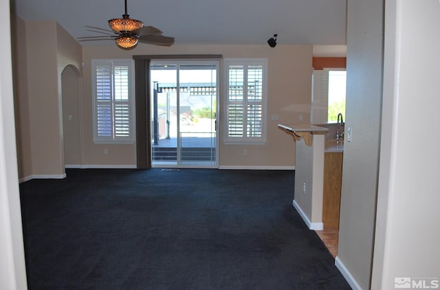 spare room with baseboards, a ceiling fan, dark carpet, and a healthy amount of sunlight