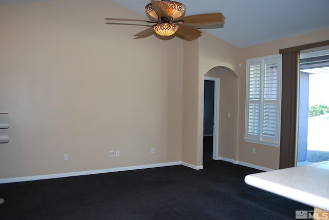 empty room with ceiling fan, arched walkways, vaulted ceiling, baseboards, and dark carpet