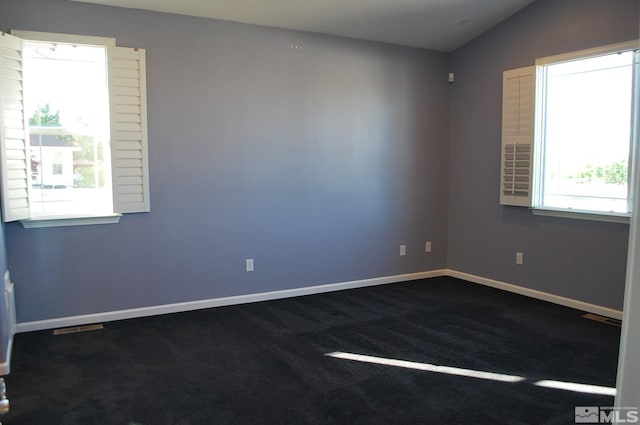 empty room featuring dark colored carpet, baseboards, lofted ceiling, and visible vents