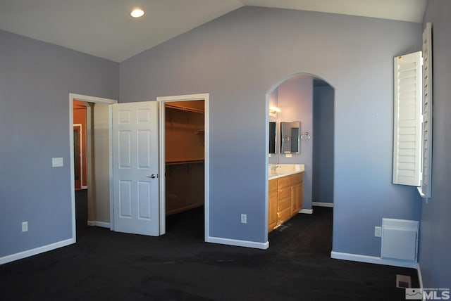 unfurnished bedroom featuring lofted ceiling, baseboards, dark carpet, a walk in closet, and arched walkways