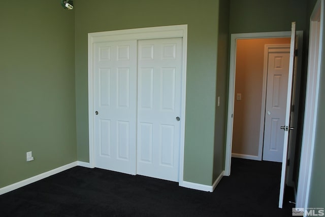 unfurnished bedroom with baseboards, dark carpet, and a closet