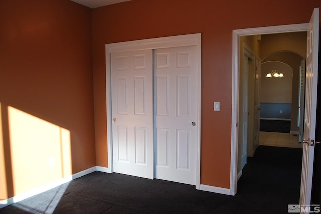 unfurnished bedroom with baseboards, a closet, dark carpet, and a chandelier