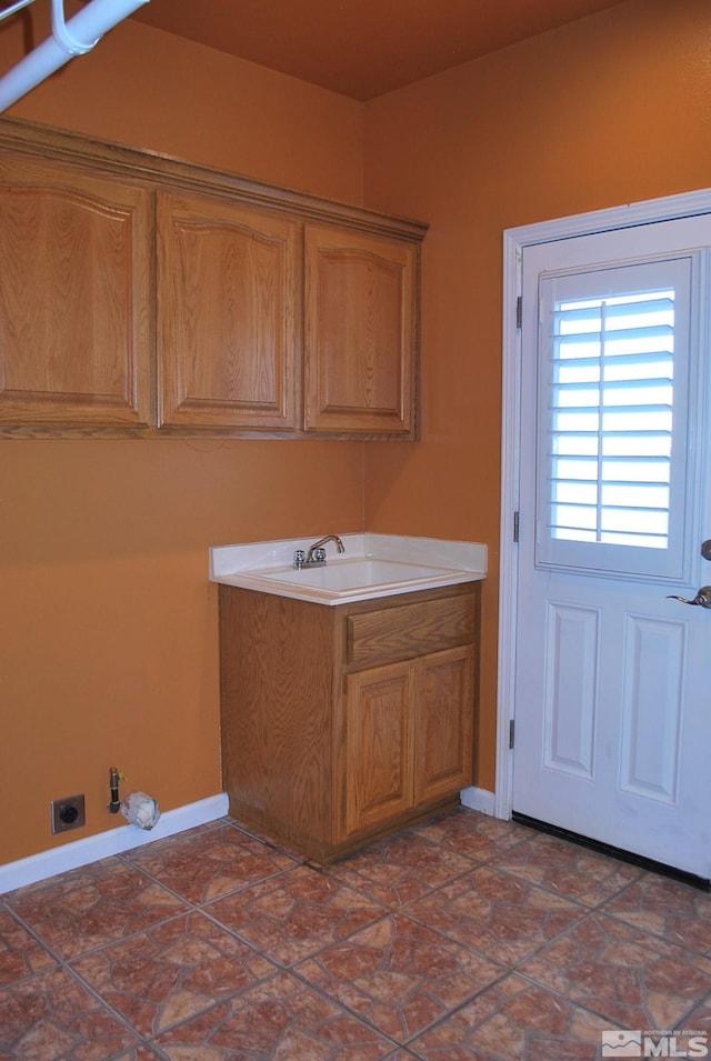 washroom featuring a sink, baseboards, hookup for an electric dryer, and cabinet space