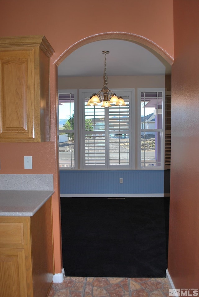 unfurnished dining area with arched walkways, baseboards, a notable chandelier, and plenty of natural light