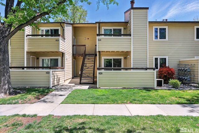 view of front of house with a front lawn, a balcony, a chimney, central AC unit, and stairway