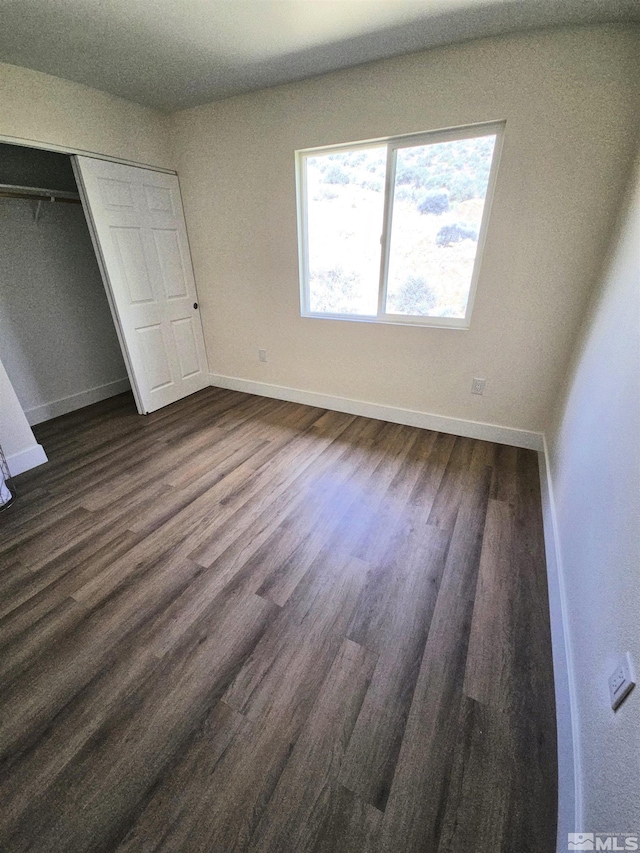 unfurnished bedroom featuring baseboards, dark wood finished floors, and a closet