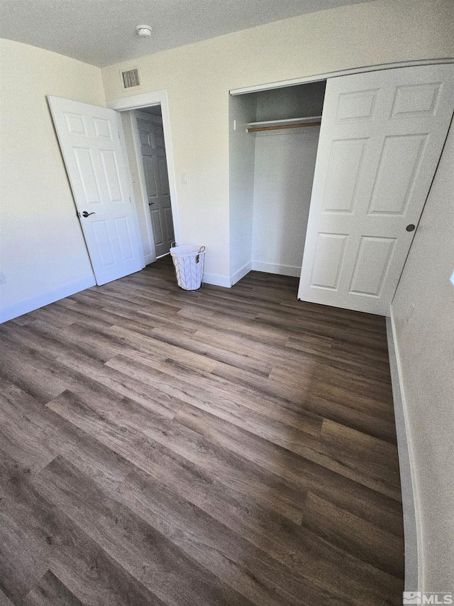 unfurnished bedroom featuring dark wood finished floors, baseboards, and a closet