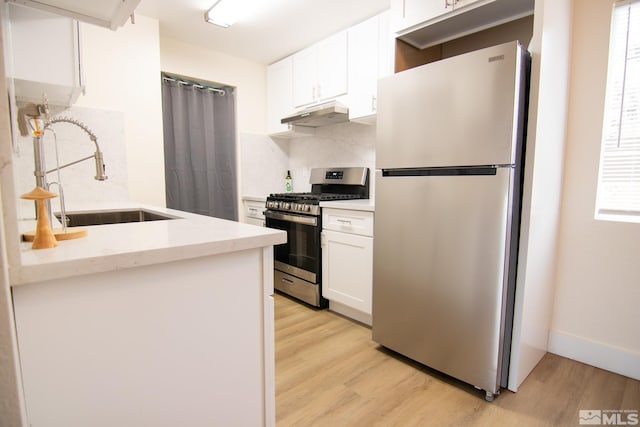 kitchen featuring stainless steel appliances, a sink, light wood finished floors, under cabinet range hood, and white cabinets