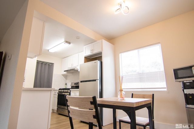 kitchen with appliances with stainless steel finishes, light wood-type flooring, white cabinets, under cabinet range hood, and light countertops